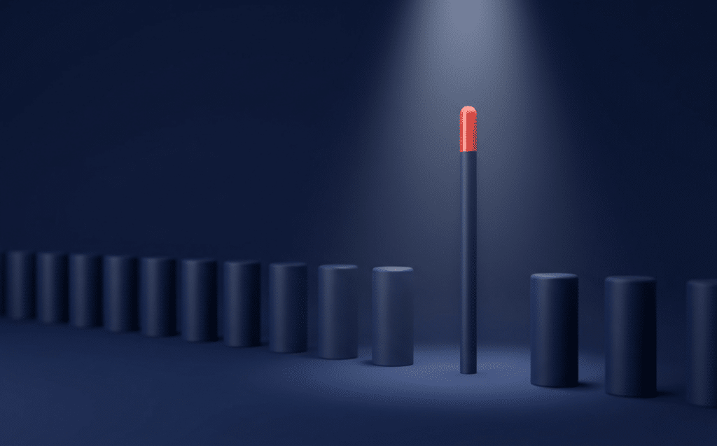 A single tall black column with a red top stands out among a row of identical shorter blue cylinders under a spotlight, conveying individuality or leadership.
